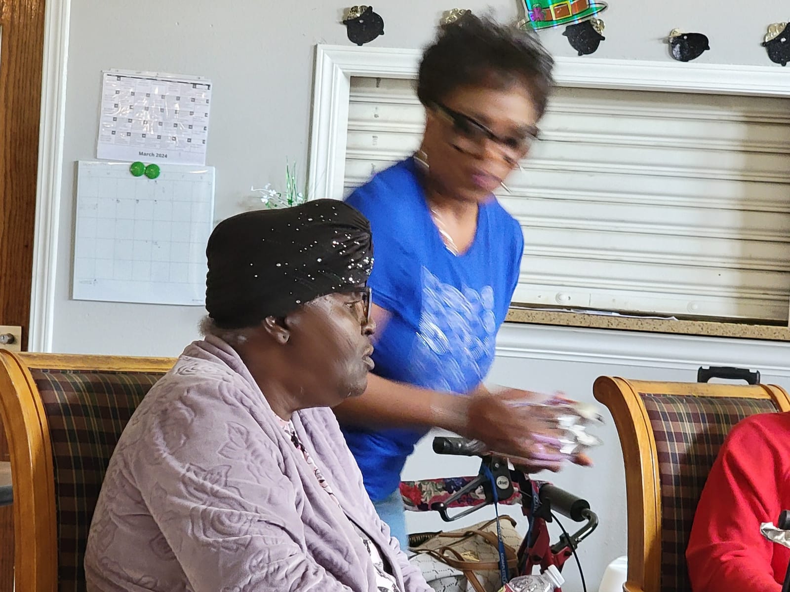 A volunteer in a blue shirt helping a senior in a wheelchair