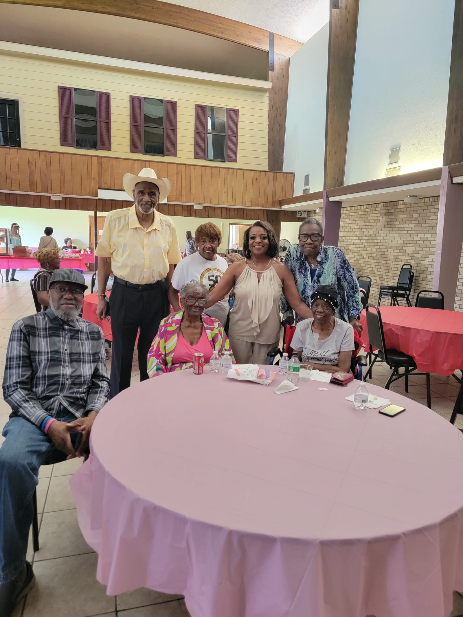 A group of seniors, one in a cowboy hat, posing around a table at a community hall