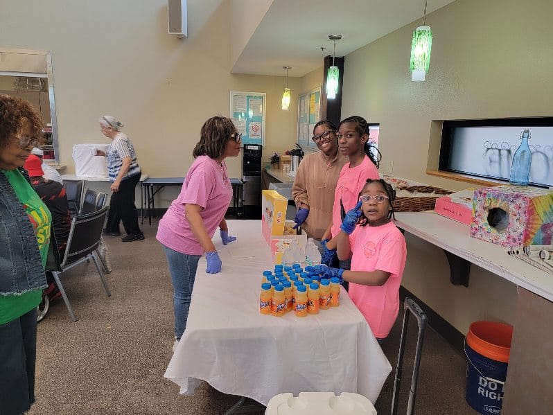 Volunteers in pink shirts and gloves setting out drinks and snacks before an event